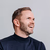Smiling man with short hair and beard wearing a dark turtleneck looking to the right.